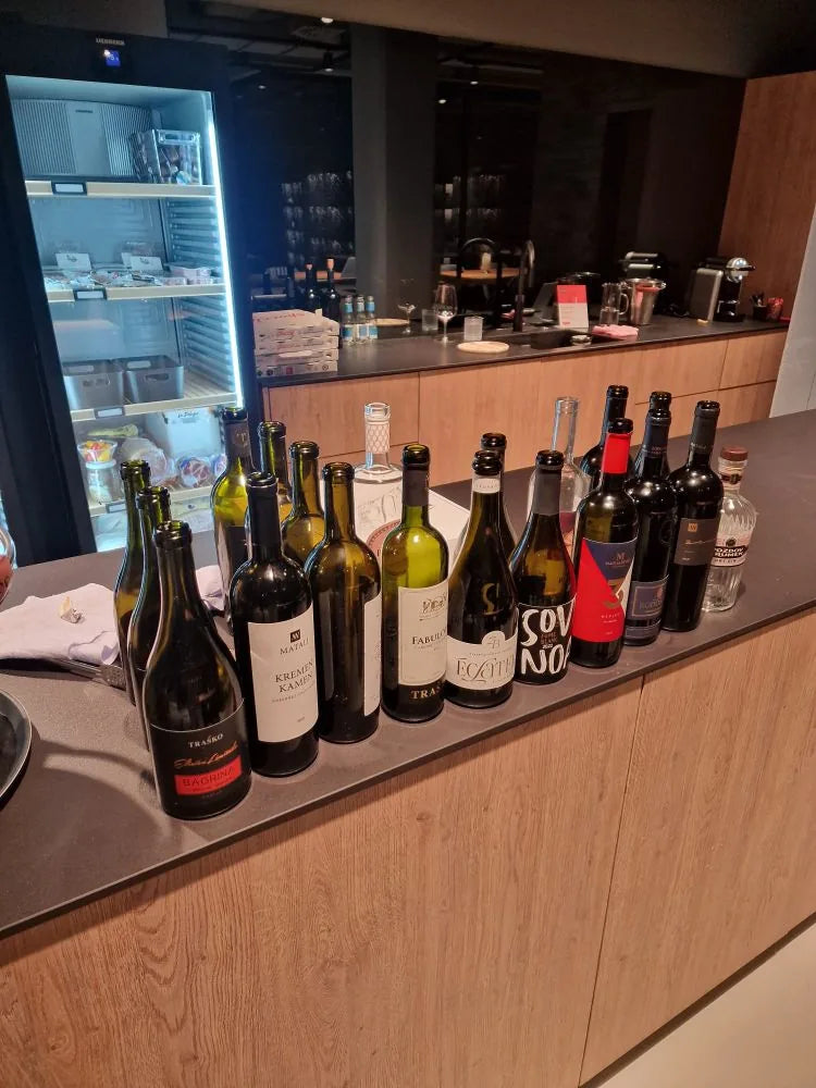 Gruppe von Wein- und Schaumweinflaschen auf der Bar aus Eichenholz, im Hintergrund ein beleuchteter Kühlschrank